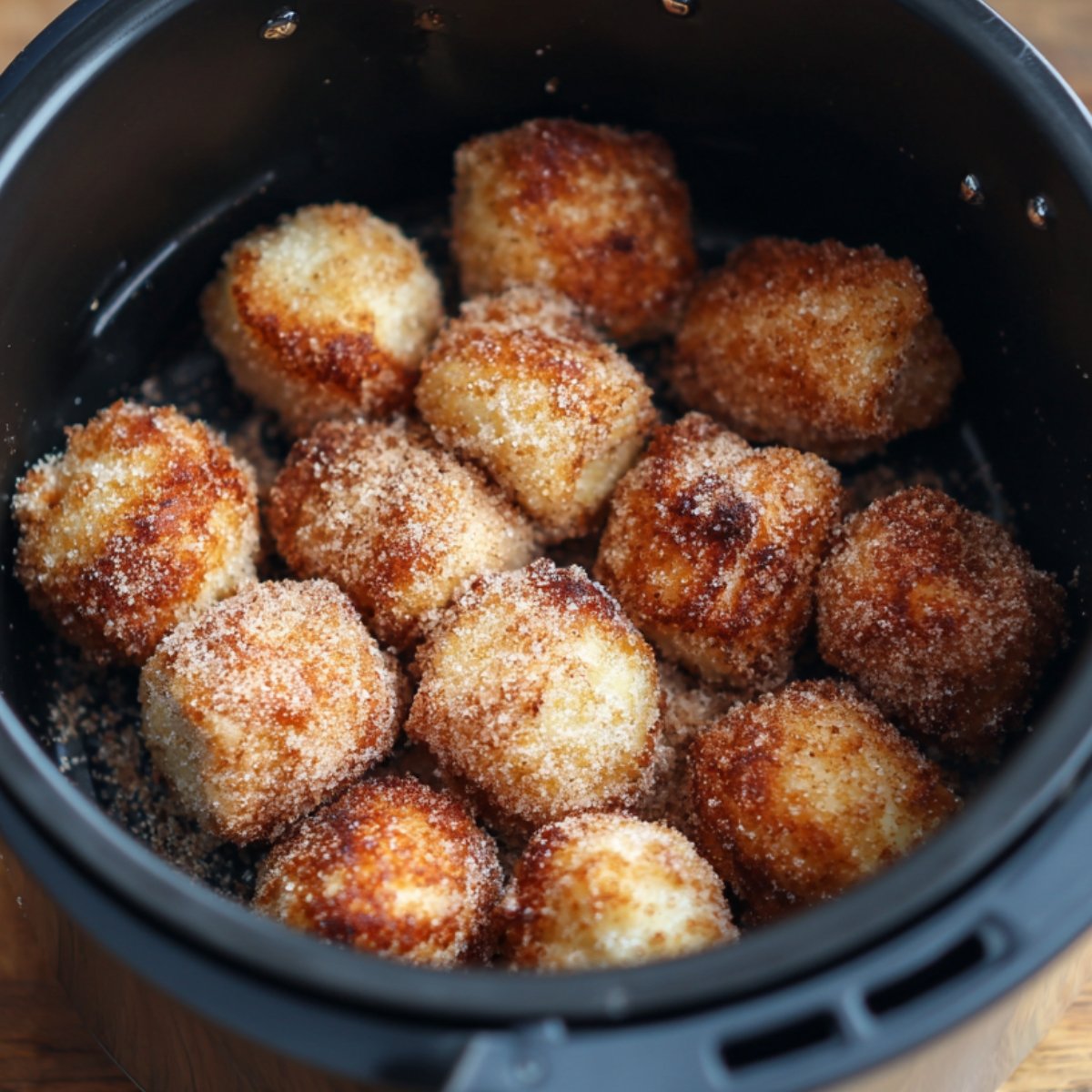 A basket lined with parchment holds a dozen sugar‑and‑cinnamon–coated dough balls, their crisp, golden surfaces flecked with fine granules of spice.