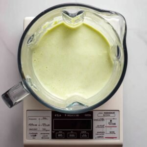 Overhead shot of the thick, pale green avocado‑banana smoothie resting in the blender pitcher