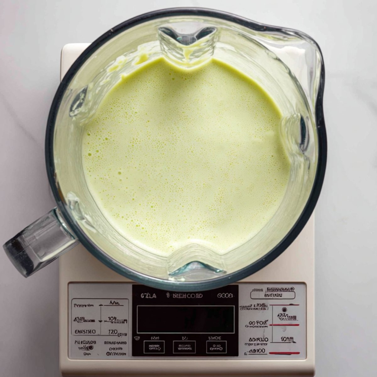 Overhead shot of the thick, pale green avocado‑banana smoothie resting in the blender pitcher