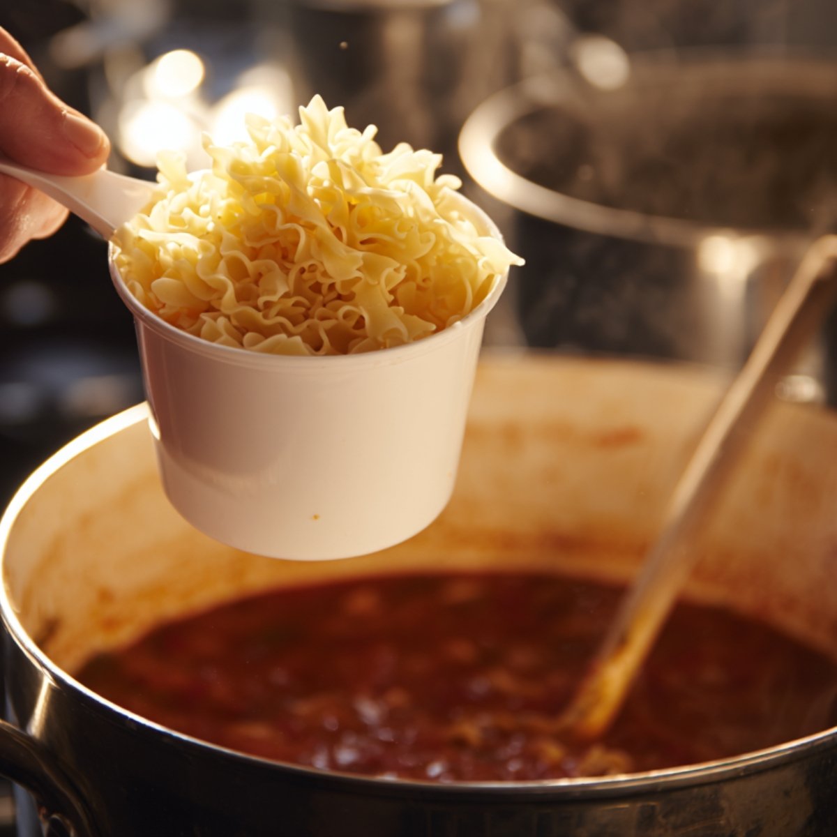 Overhead shot of a spoon lifting a gooey strand of melted cheese and pasta from a bowl of lasagna soup, revealing the rich tomato broth and chopped herbs below.