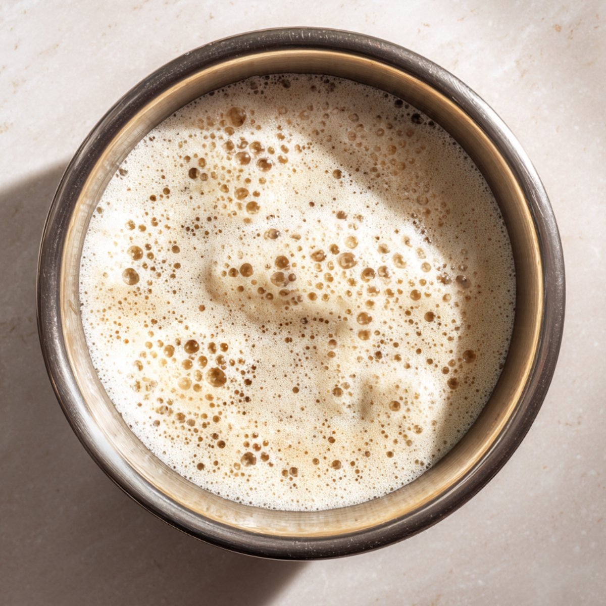 Top-down shot of a foamy, activated yeast mixture in a metal bowl