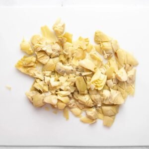 Chopped marinated artichoke hearts piled on a white plastic cutting board.