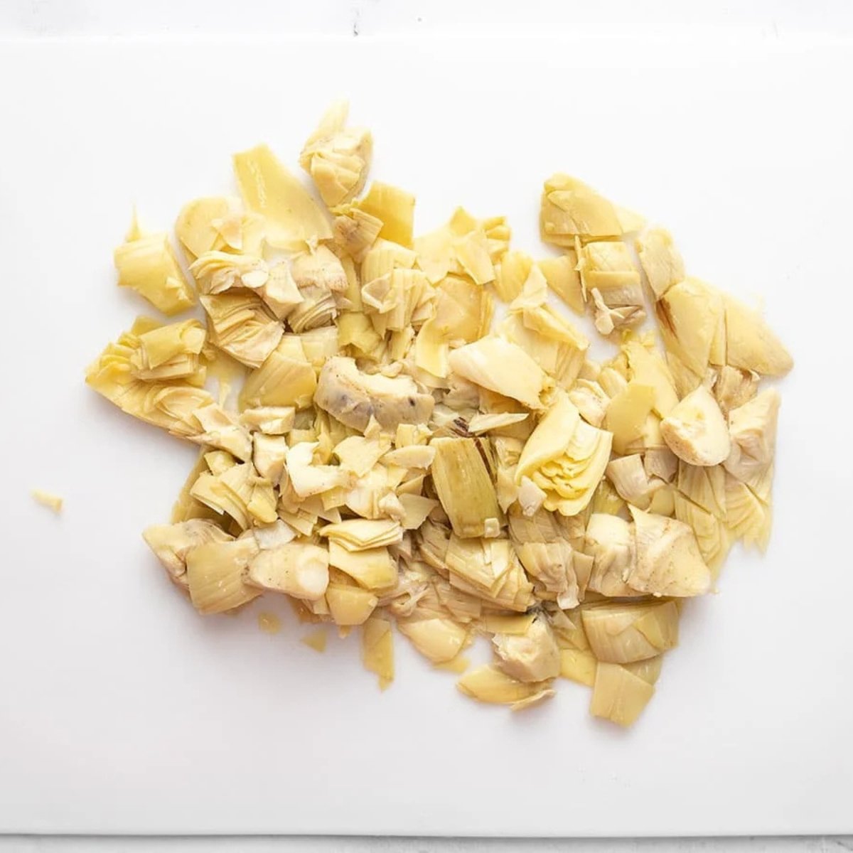 Chopped marinated artichoke hearts piled on a white plastic cutting board.