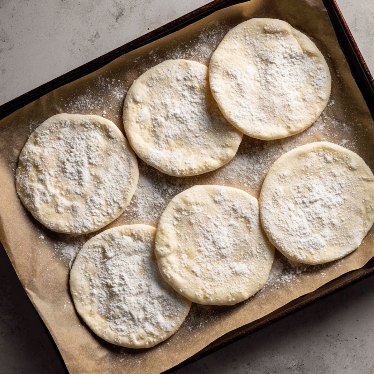 Six lightly floured, oval naan discs laid out on parchment‑lined baking sheets, ready to cook.