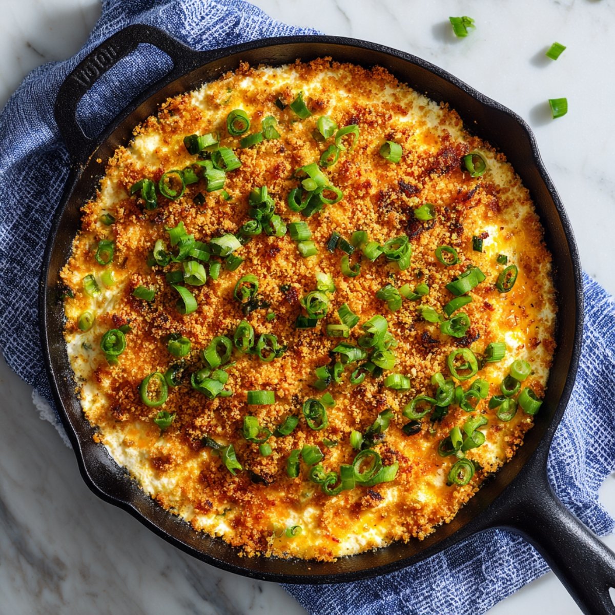 A pale blue ceramic bowl of creamy, orange-hued buffalo chicken dip topped with melted cheddar, set on a round white platter with square crackers and celery sticks. A hand reaches in with a cracker scoop, and two turquoise glasses and a folded napkin sit nearby.