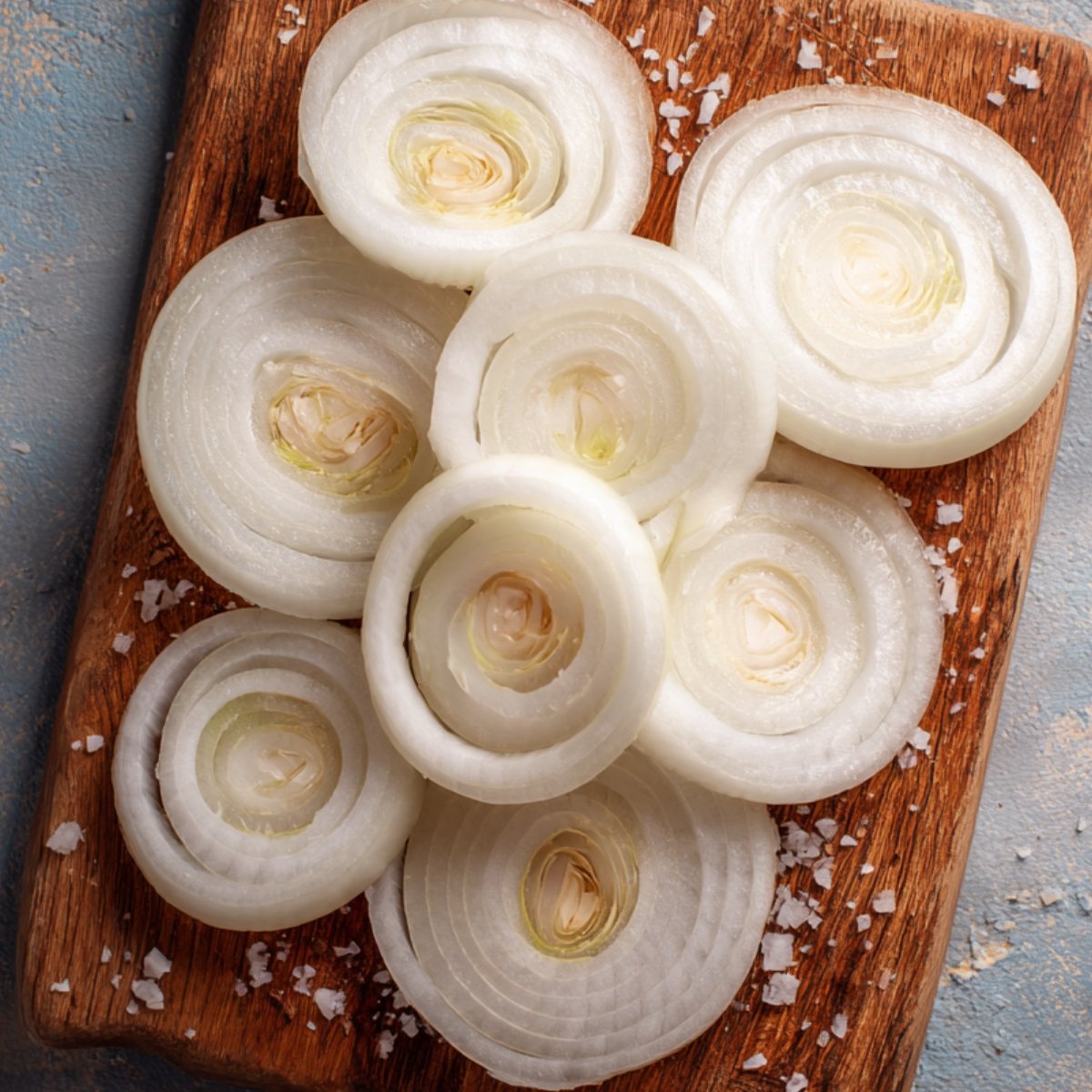 Thick slices of sweet white onion arranged on a wooden board, papery skins removed, sprinkled with coarse salt.