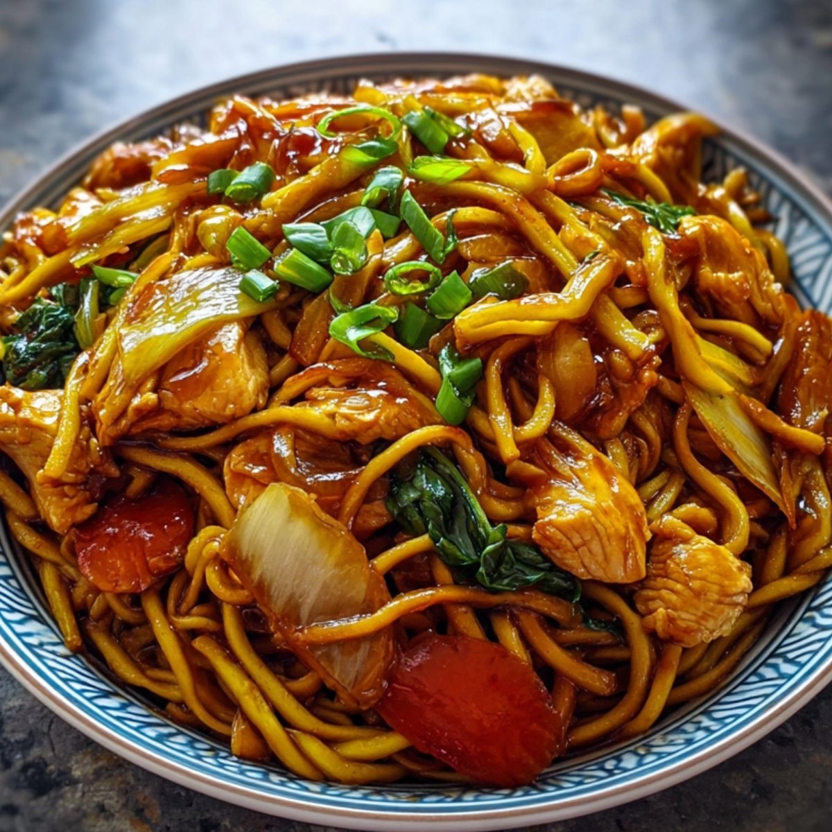 A savory dish of stir-fried noodles with Chicken Chow Mein, tossed in a rich soy-based sauce, mixed with vegetables like onions, carrots, and leafy greens, and garnished with chopped green onions. Served in a patterned bowl.