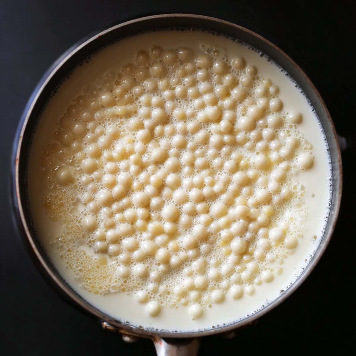 A pot filled with tapioca pearls simmering in milk, with the pearls floating on the surface.