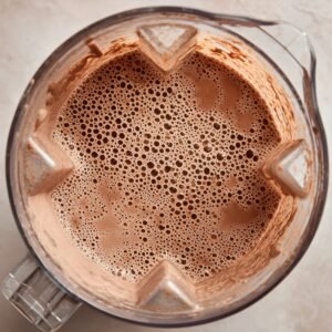 Top-down view of a blender filled with frothy, well-blended chocolate Oreo milkshake, showing a smooth and bubbly texture around the edges