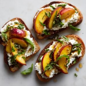 Toasted bread topped with whipped ricotta, fresh peach slices, basil leaves, and a drizzle of honey and balsamic glaze.