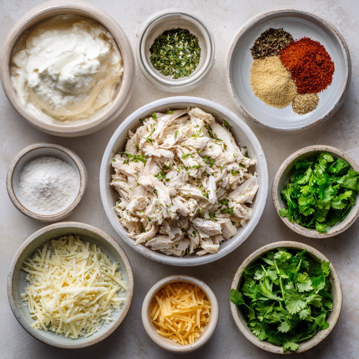 Overhead view of shredded chicken, herbs, shredded cheese, sour cream, and seasoning for enchilada filling.