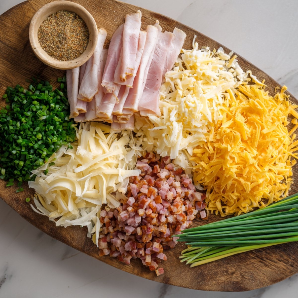 A wooden board filled with chopped and shredded cheese (cheddar, mozzarella), cubed ham and bacon, fresh chives, and a bowl of seasoning, showcasing optional mix-ins for baked feta eggs or breakfast dishes.